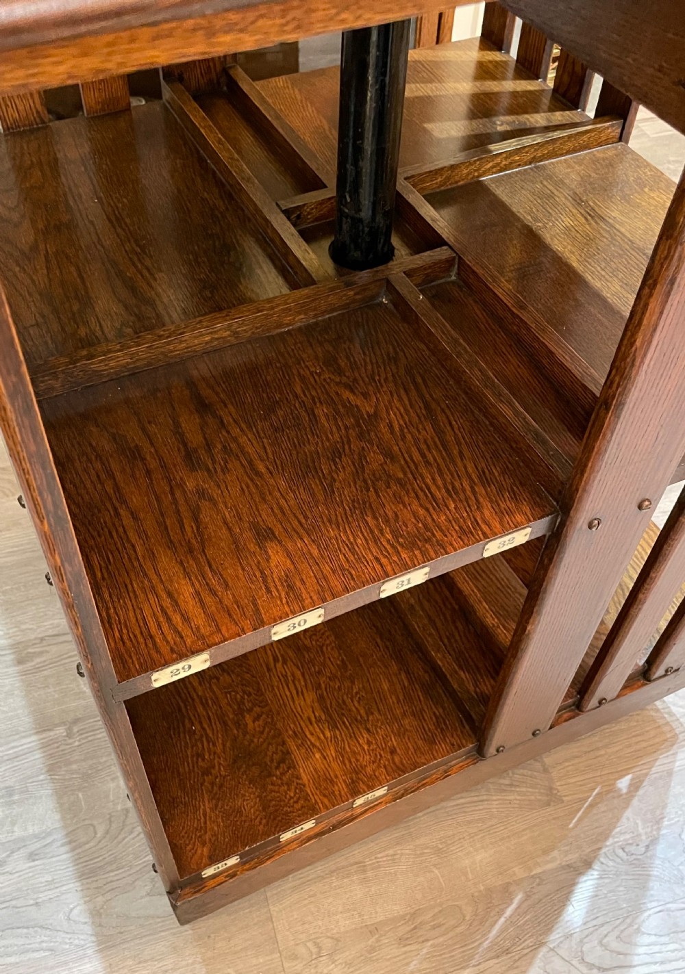 A multi-tiered Edwardian dark oak revolving bookcase with vertical side slats, upper gallery spindles, and small numbered tags along the shelf edges. View III