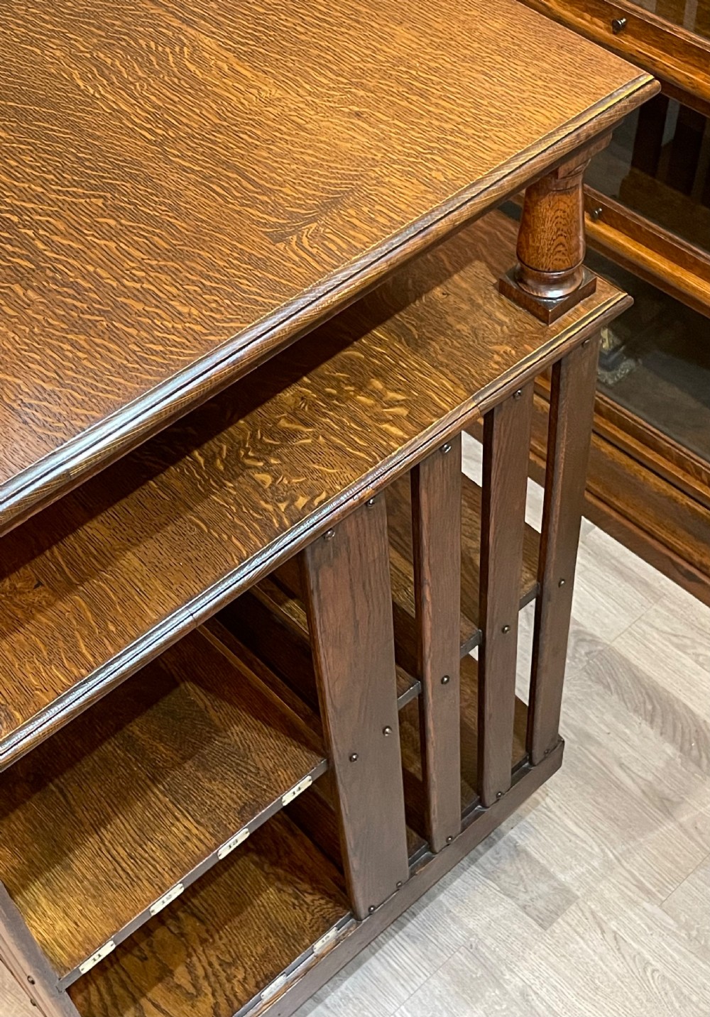 A multi-tiered Edwardian dark oak revolving bookcase with vertical side slats, upper gallery spindles, and small numbered tags along the shelf edges. View V