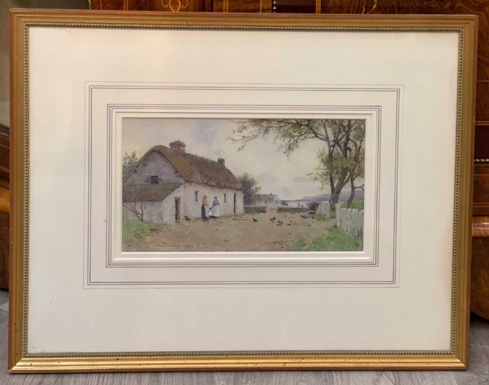 A framed watercolour painting depicting a whitewashed thatched cottage and figures near the coast, displayed within a cream wash-line mount and a gold frame.