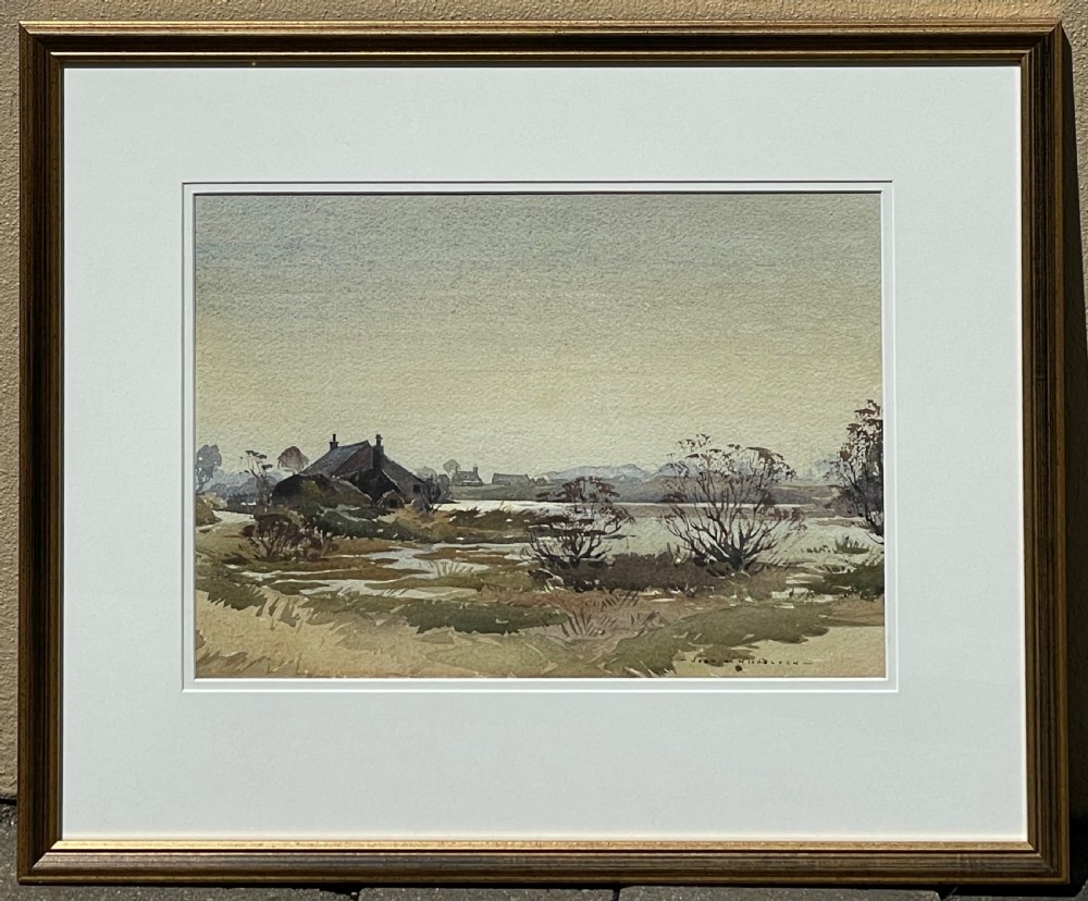 A framed horizontal watercolour painting depicting a rural cottage and marshland landscape under a soft grey sky.