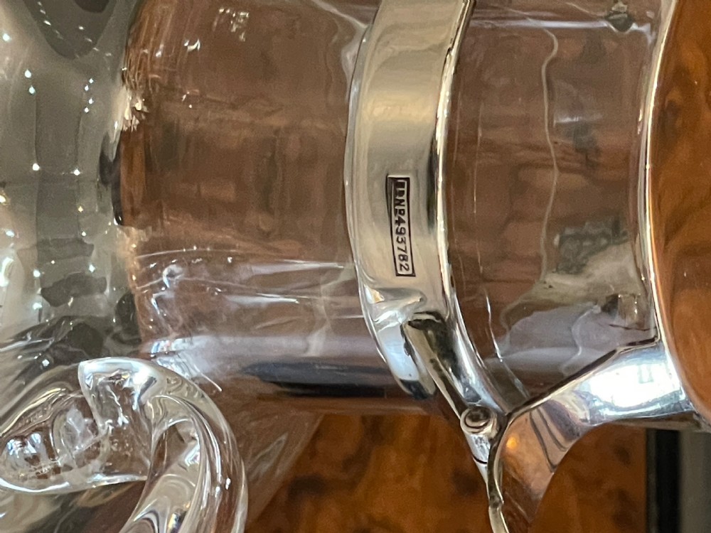 An Edwardian clear glass claret jug featuring a bulbous body, an integrated glass handle, and a polished silver-plated collar with a hinged spout lid. View III