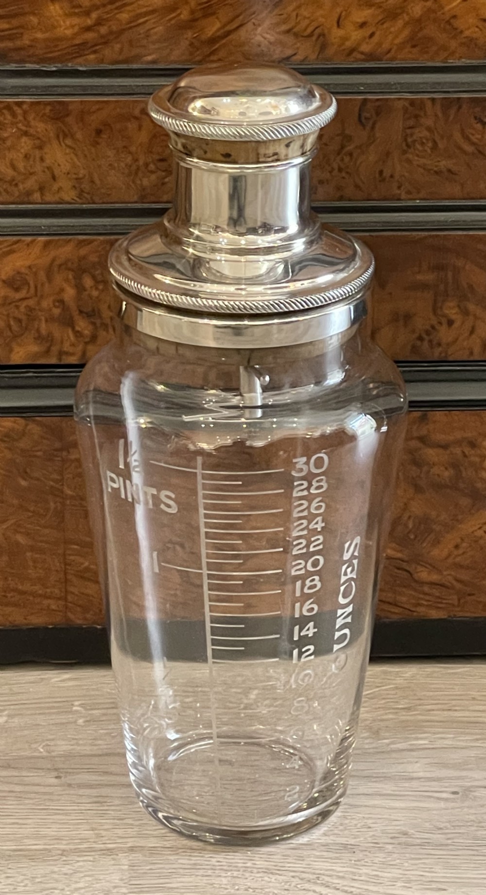 An Art Deco clear glass cocktail shaker featuring etched pint and ounce measurements and a silver-plated stopper.