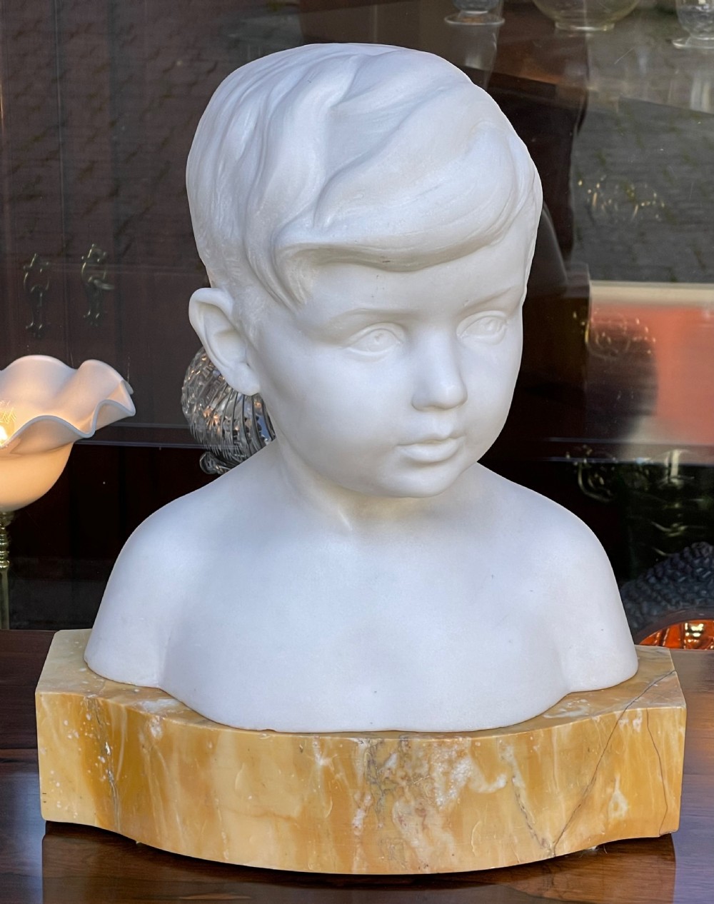 A white Carrara marble sculpture depicting the bust of a young boy, mounted on a yellow variegated marble base. View II