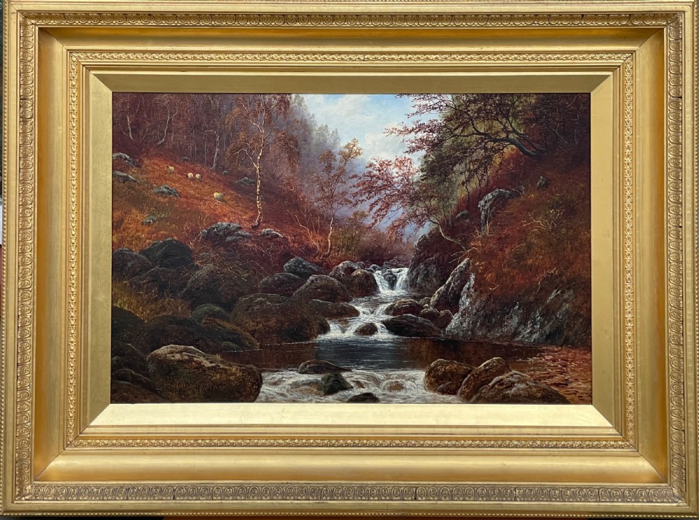 An antique oil painting depicting a rocky woodland river with a waterfall and sheep on an autumnal hillside, enclosed in a gilded frame.
