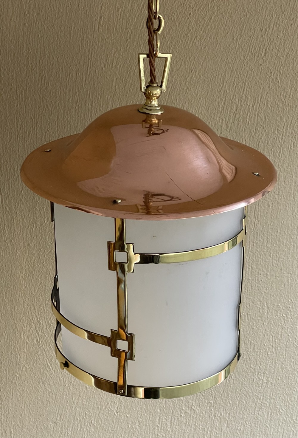 An Art Deco pendant lantern featuring a polished copper dome top, geometric brass frame, cylindrical frosted glass shade, and hanging chain. View IV