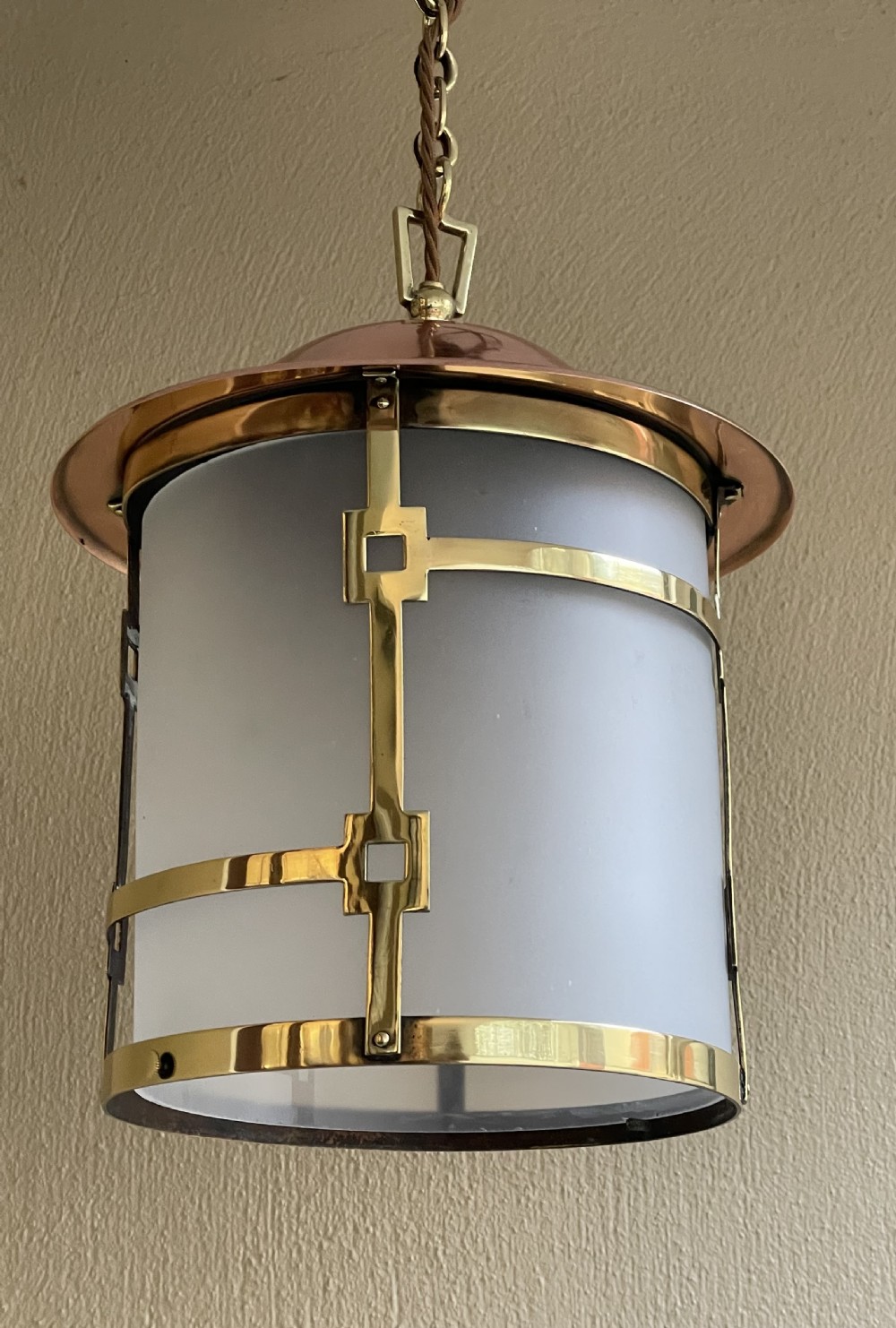 An Art Deco pendant lantern featuring a polished copper dome top, geometric brass frame, cylindrical frosted glass shade, and hanging chain. View V