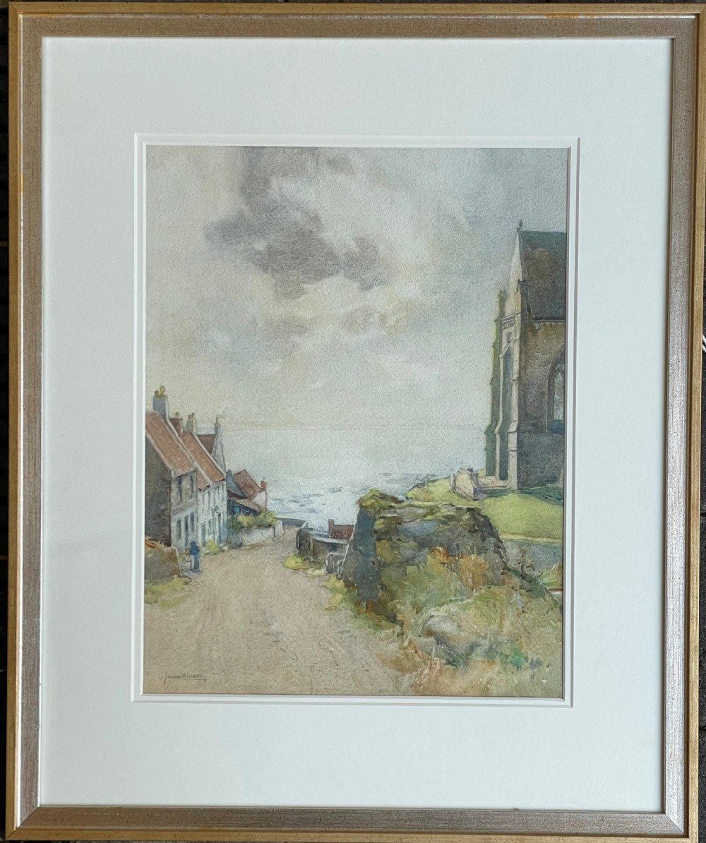 A framed watercolour painting depicting a village road leading down toward the sea, flanked by stone cottages on the left and a church on the right under a cloudy sky.