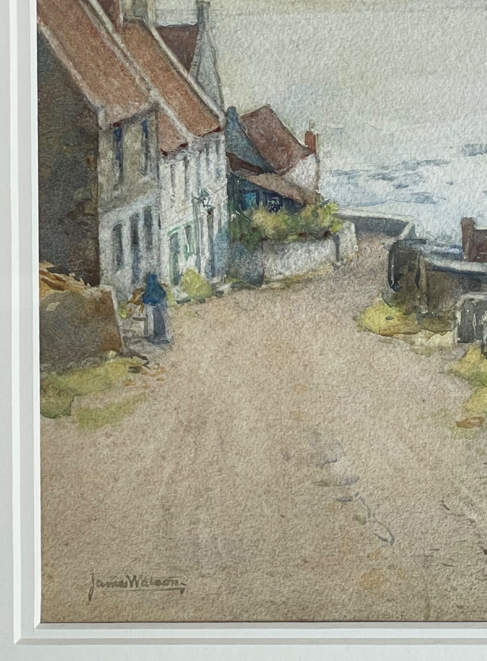 A framed watercolour painting depicting a village road leading down toward the sea, flanked by stone cottages on the left and a church on the right under a cloudy sky. View II
