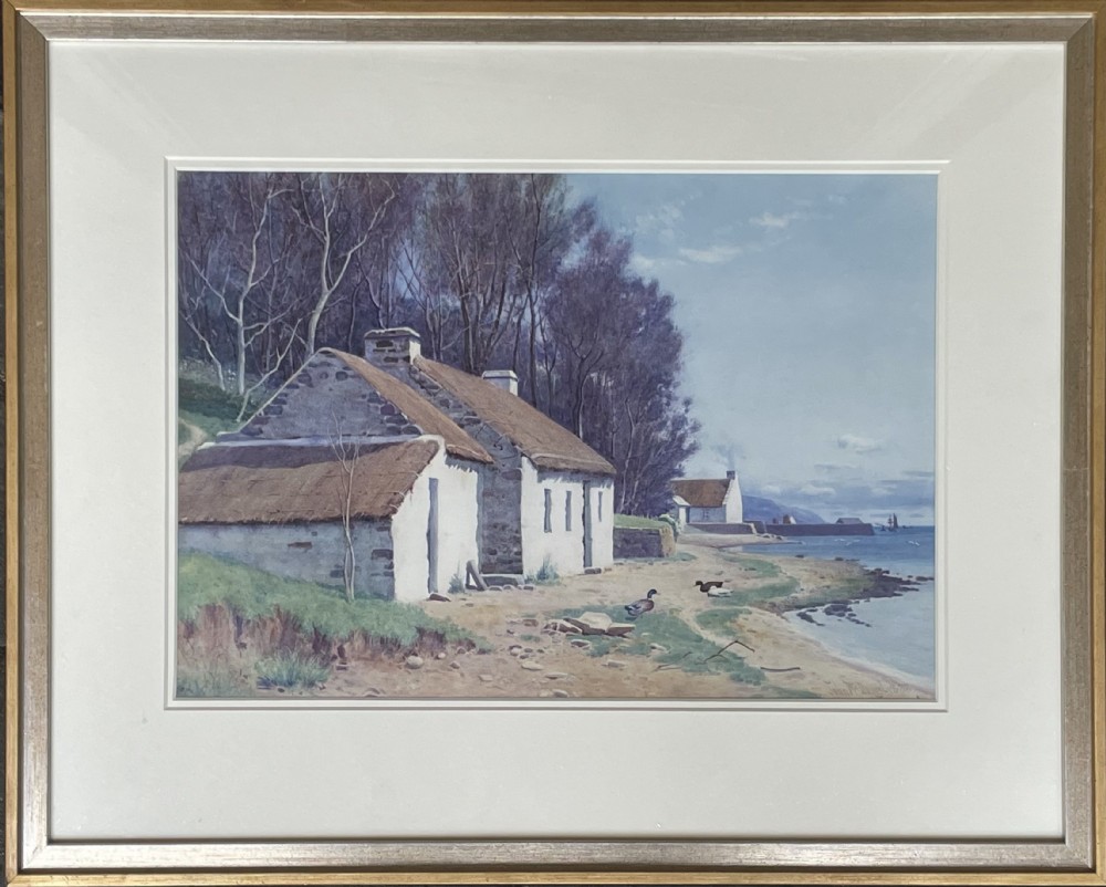 A framed watercolour painting featuring whitewashed thatched cottages on a coastal shore beside a blue sea, presented in a light-coloured mount and silver frame.