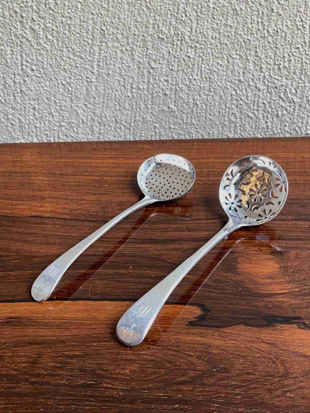 Two Georgian sterling silver sifter spoons displaying hand-pierced bowl patterns and engraved handle terminals.