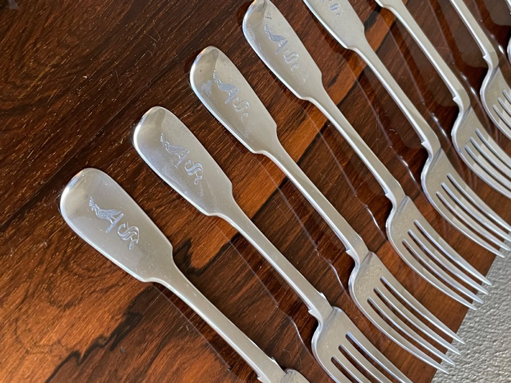 A set of nine antique Irish sterling silver dinner forks featuring fiddle pattern handles with engraved crests arranged on a dark wooden surface. View II