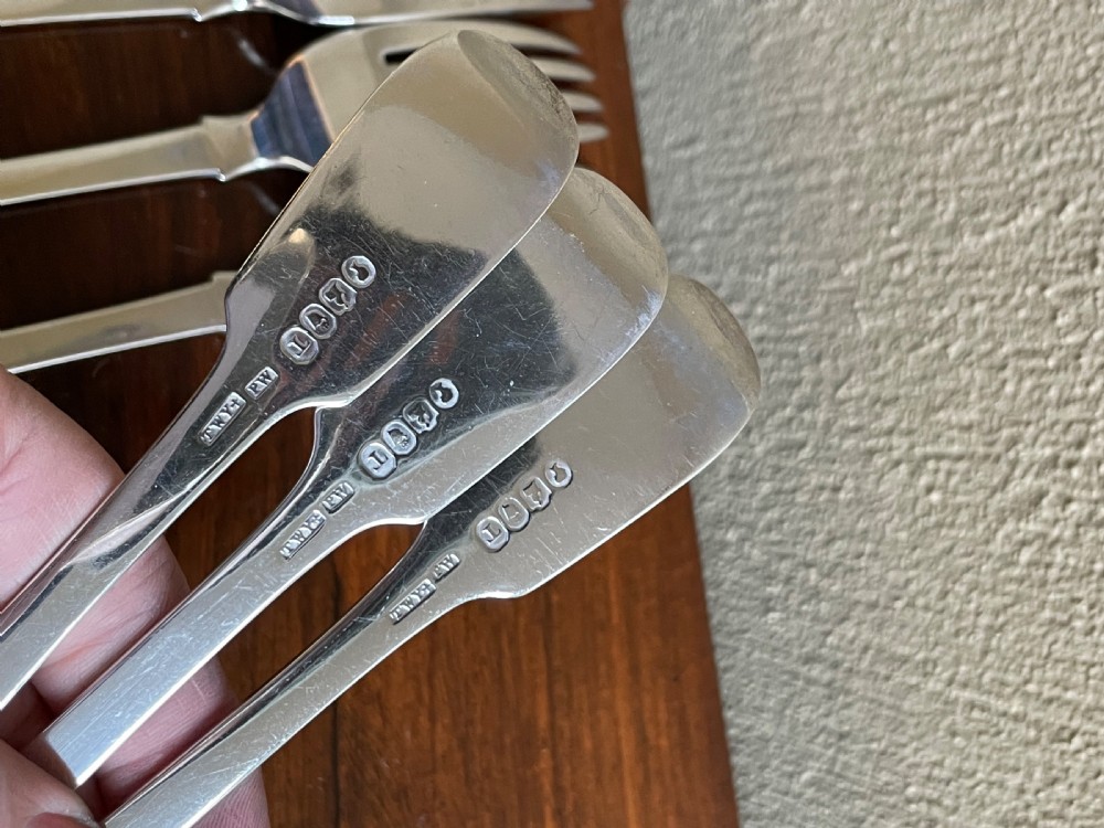 A set of nine antique Irish sterling silver dinner forks featuring fiddle pattern handles with engraved crests arranged on a dark wooden surface. View IV