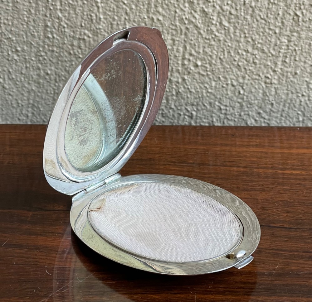 An oval silver compact featuring an engraved landscape scene with junk boats, mountains, trees, and a textured background. View III