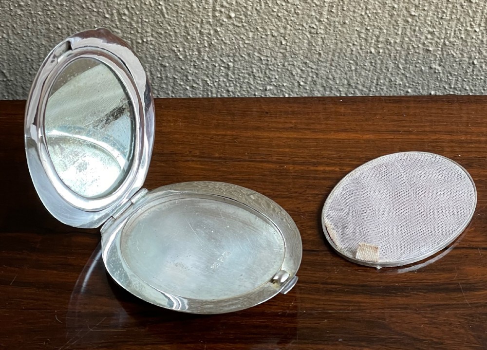 An oval silver compact featuring an engraved landscape scene with junk boats, mountains, trees, and a textured background. View IV