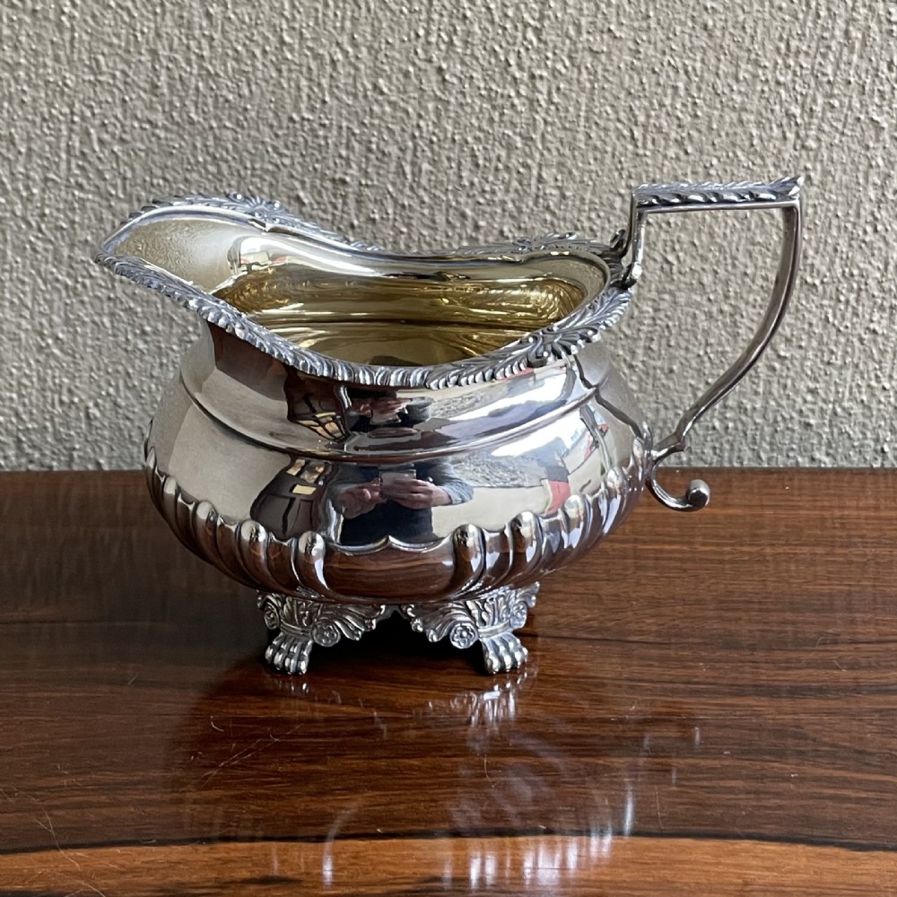 An Edwardian silver cream jug featuring a fluted lower body, cast shell feet, a gadrooned rim, and a gilded interior.