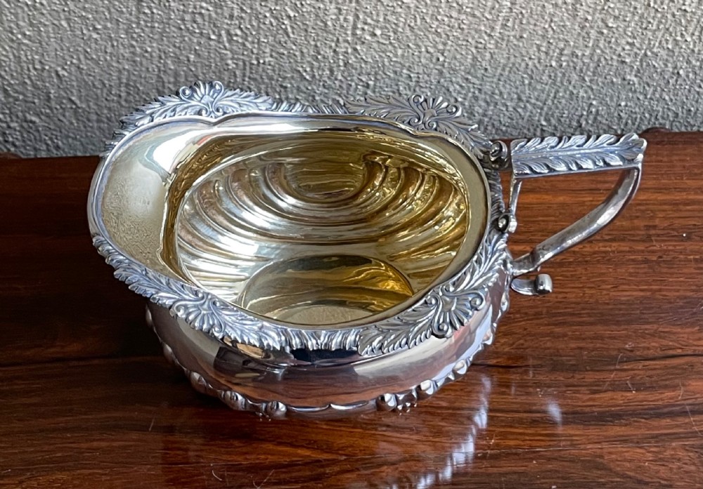 An Edwardian silver cream jug featuring a fluted lower body, cast shell feet, a gadrooned rim, and a gilded interior. View II
