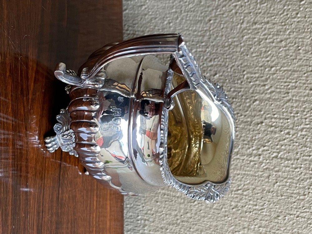 An Edwardian silver cream jug featuring a fluted lower body, cast shell feet, a gadrooned rim, and a gilded interior. View V
