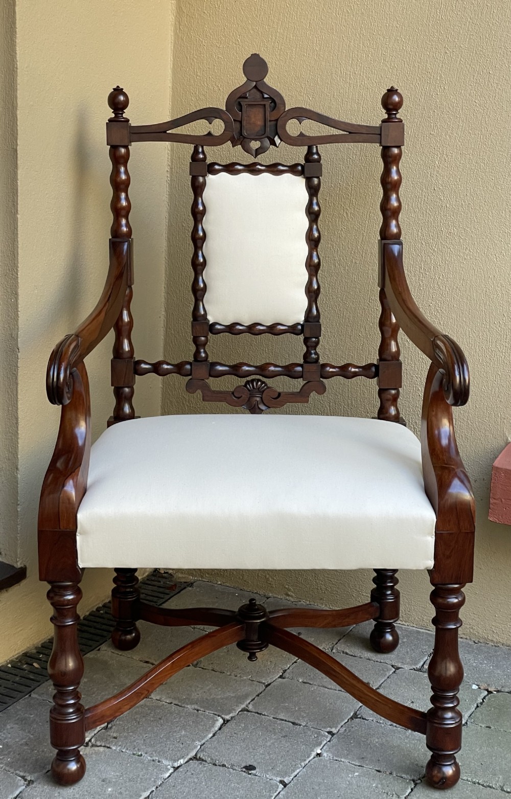 An early Victorian rosewood library chair with bobbin-turned supports, scroll armrests, cream upholstery, and a curved X-stretcher base.