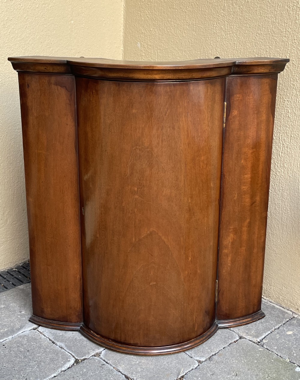 A late nineteenth-century mahogany bowfront corner cupboard with a central curved door and side panels.