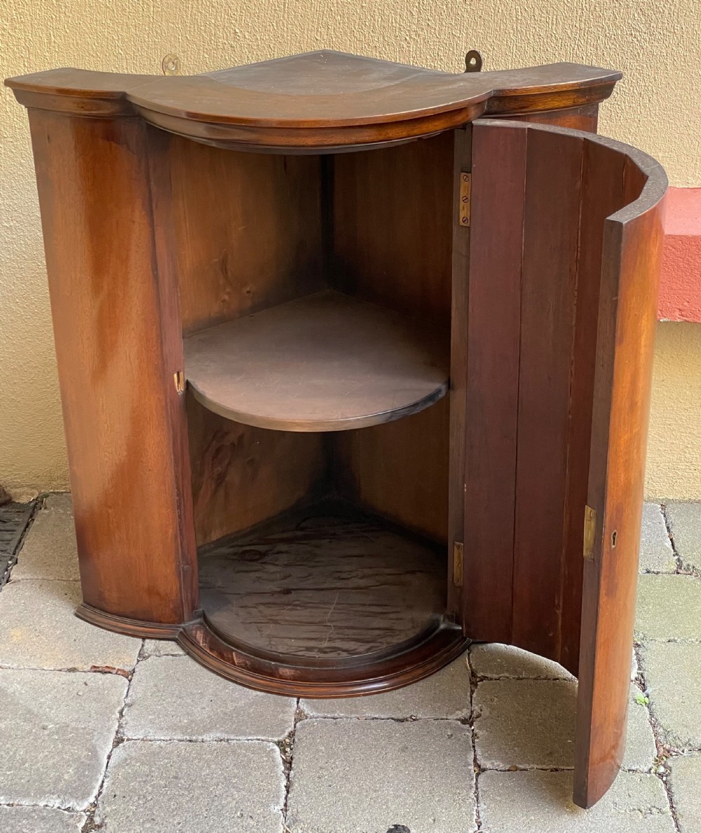 A late nineteenth-century mahogany bowfront corner cupboard with a central curved door and side panels. View IV