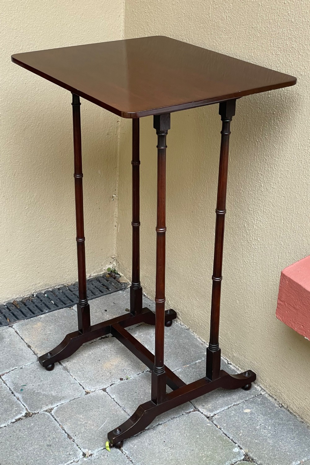 A tall, slender dark mahogany Regency end table featuring a rectangular polished top, turned supports, and a trestle base.