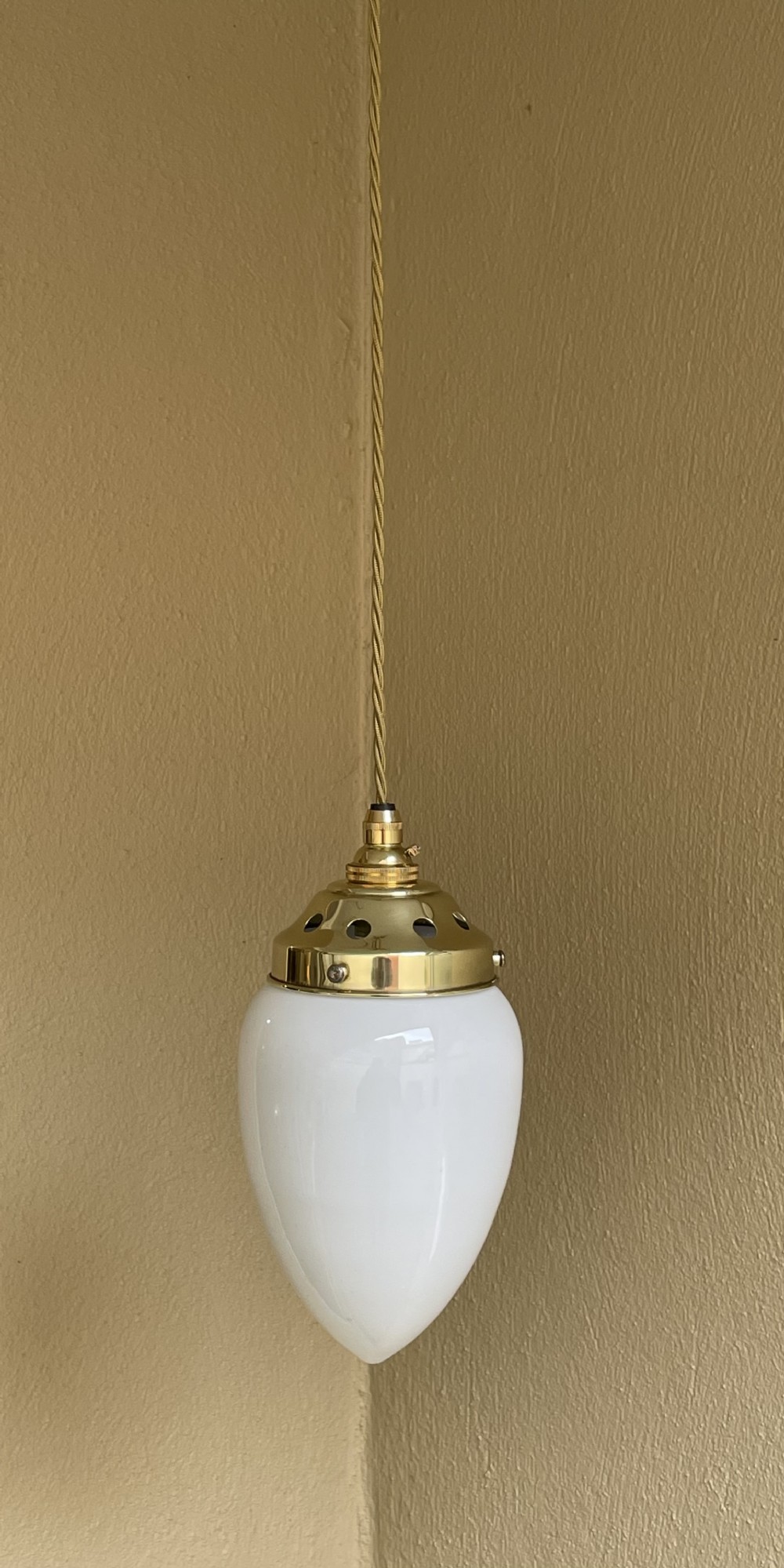 A white pear-shaped opaline glass pendant light suspended by a polished brass gallery and twisted fabric flex cord.
