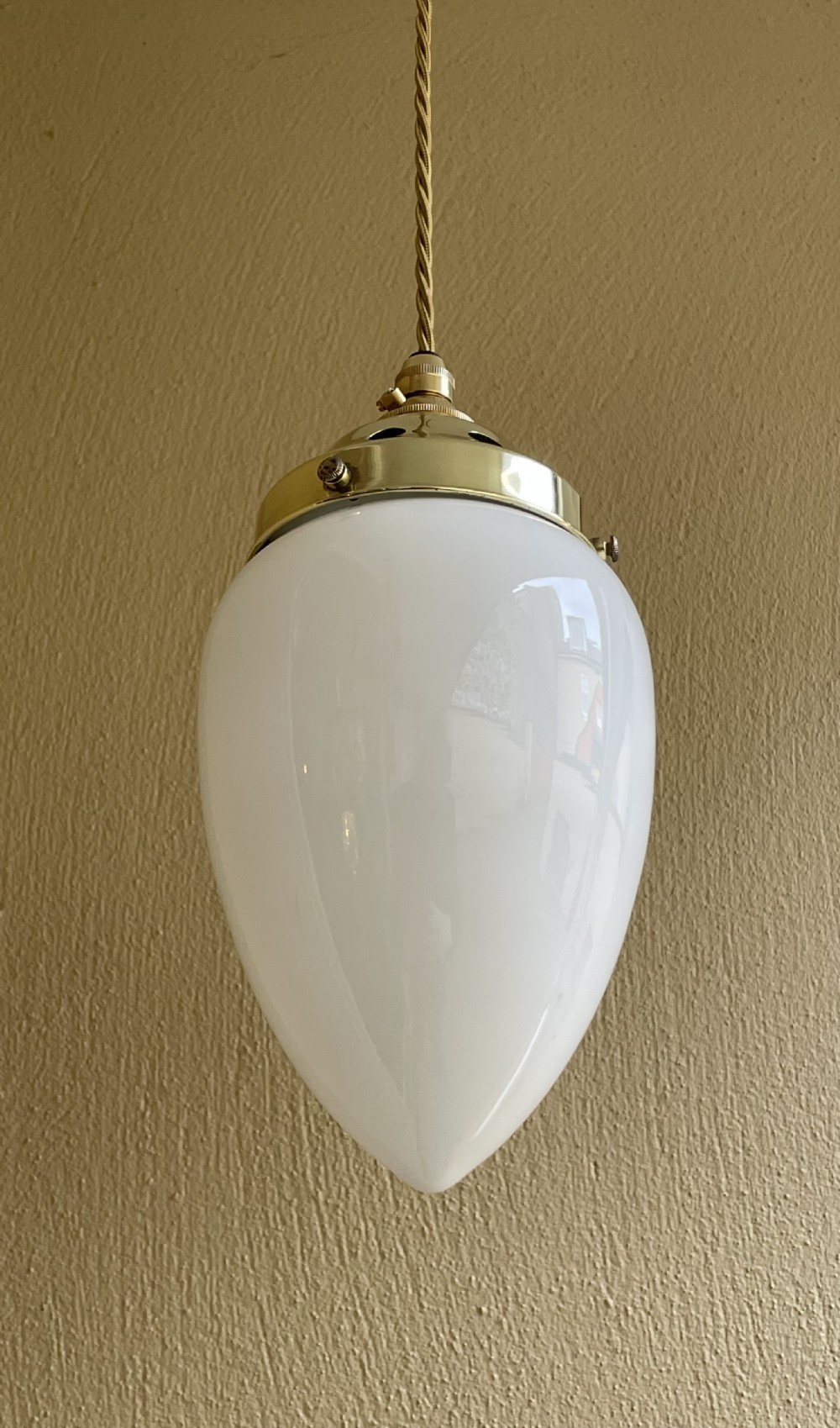 A white pear-shaped opaline glass pendant light suspended by a polished brass gallery and twisted fabric flex cord. View II