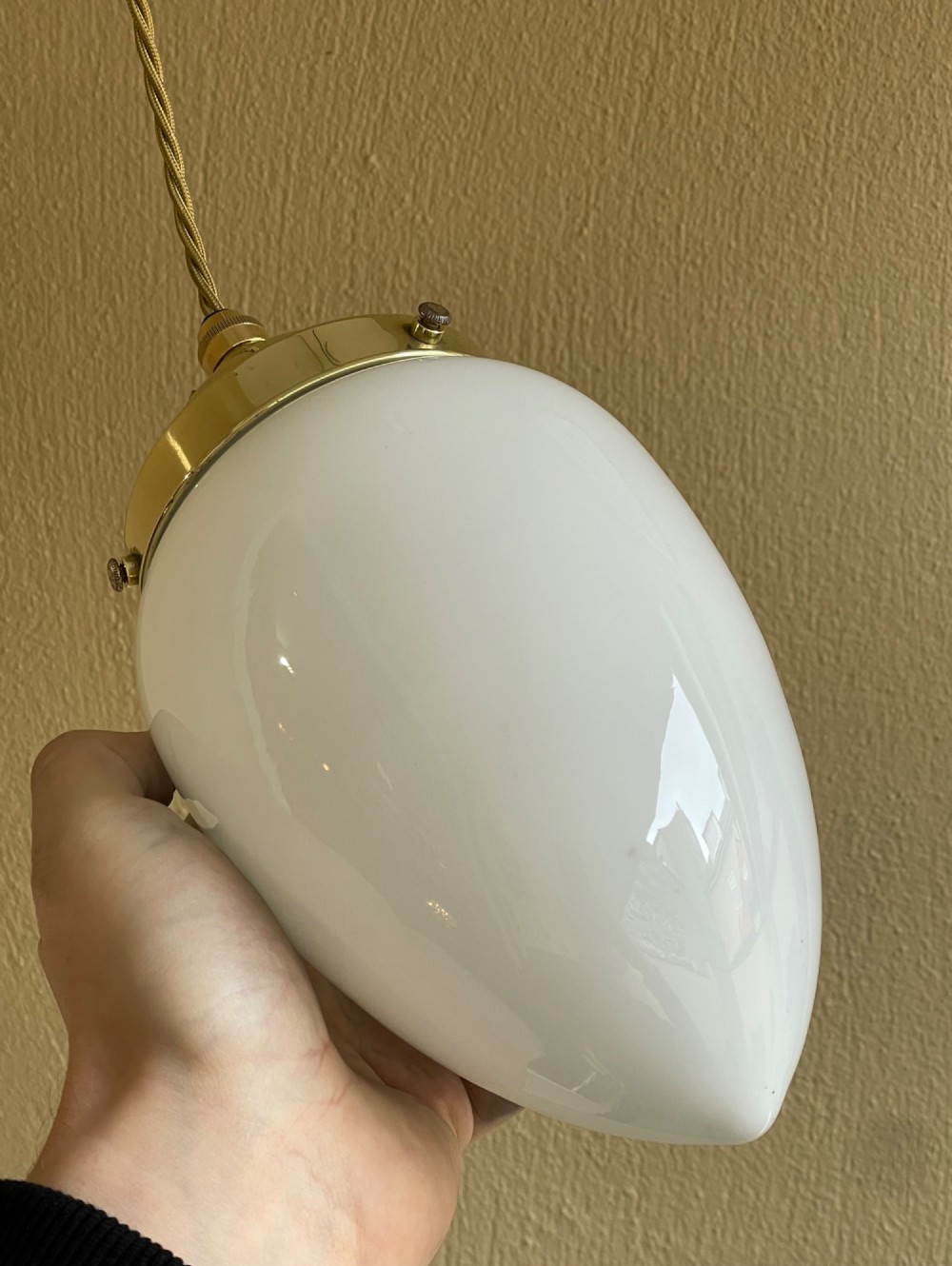 A white pear-shaped opaline glass pendant light suspended by a polished brass gallery and twisted fabric flex cord. View III