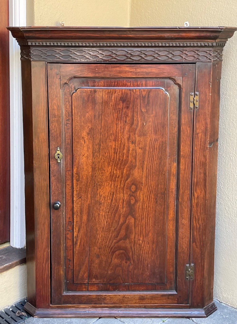 A Georgian red walnut corner cupboard with a carved geometric frieze, moulded cornice, single fielded door panel, and brass keyhole escutcheon.