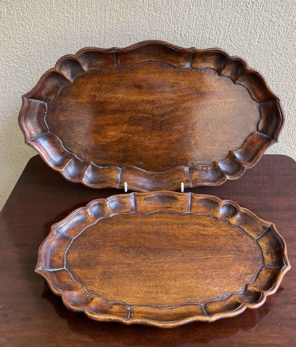 A pair of oval mahogany trays featuring carved scalloped piecrust borders and a dark polished timber finish.