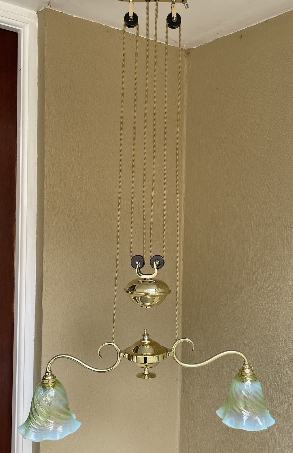 An Art Nouveau polished brass rise and fall ceiling light featuring two scrolling arms with green opalescent fluted glass shades and a central counterweight pulley system.