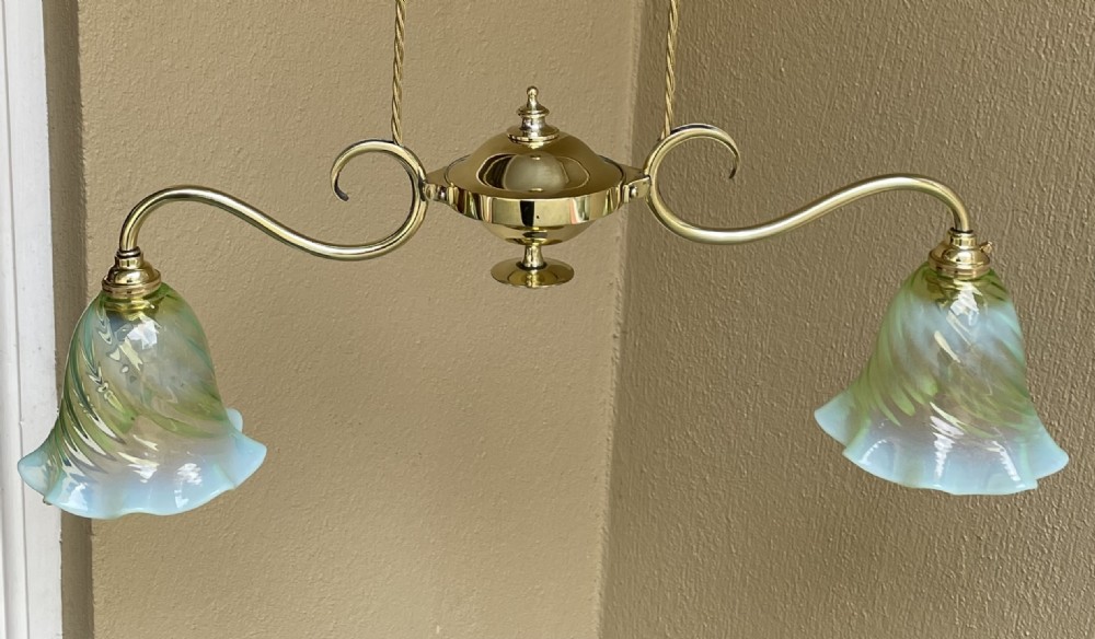 An Art Nouveau polished brass rise and fall ceiling light featuring two scrolling arms with green opalescent fluted glass shades and a central counterweight pulley system. View II