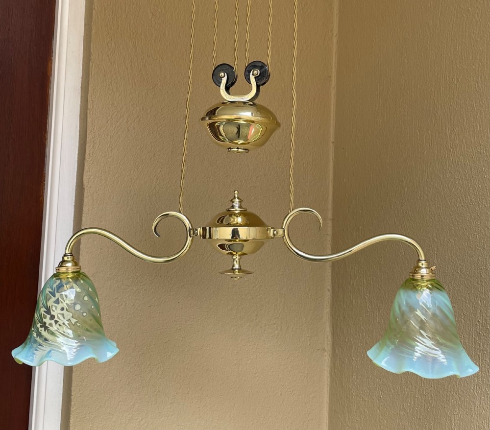 An Art Nouveau polished brass rise and fall ceiling light featuring two scrolling arms with green opalescent fluted glass shades and a central counterweight pulley system. View III