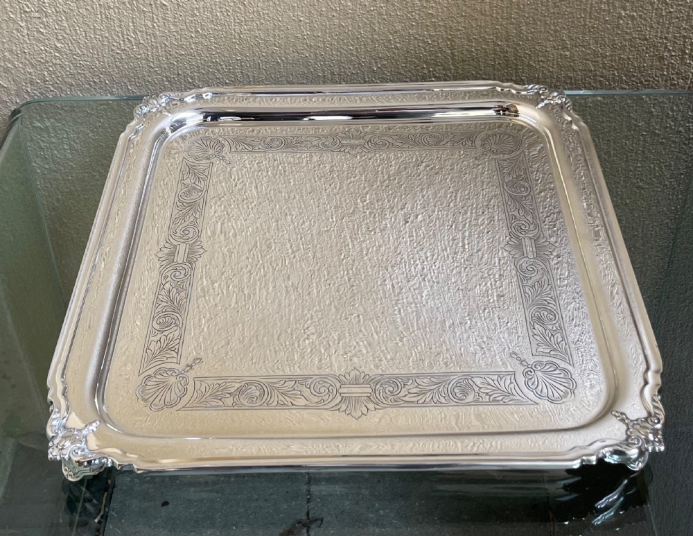 A square solid silver tray featuring hand-engraved scrollwork borders, shell corner accents, and a polished metallic surface.