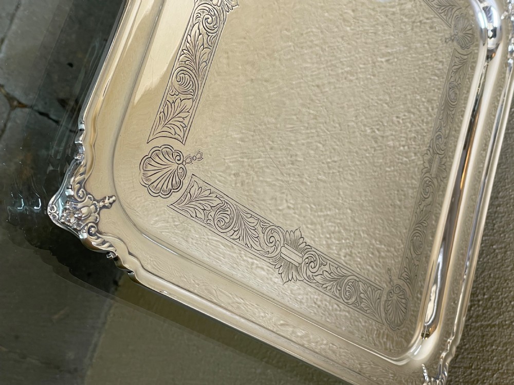 A square solid silver tray featuring hand-engraved scrollwork borders, shell corner accents, and a polished metallic surface. View V