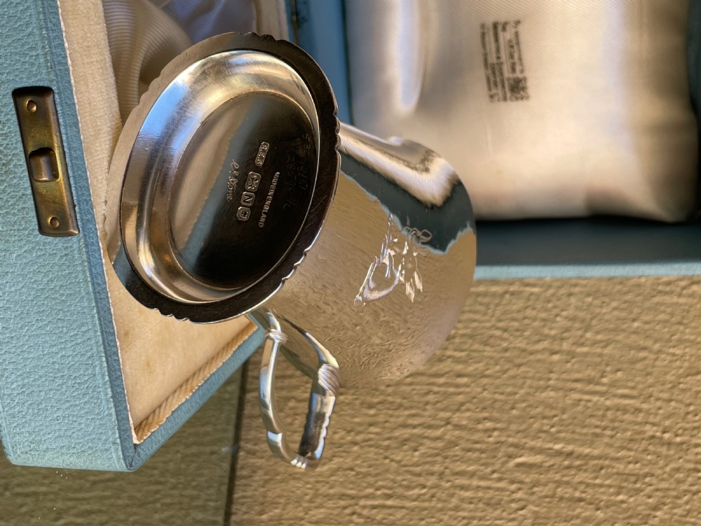 A tapered sterling silver christening mug with an engraved rabbit motif resting inside a light blue presentation case. View III