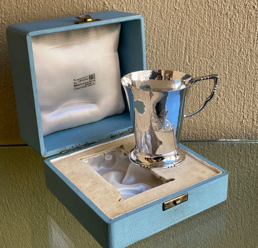 A tapered sterling silver christening mug with an engraved rabbit motif resting inside a light blue presentation case. View IV