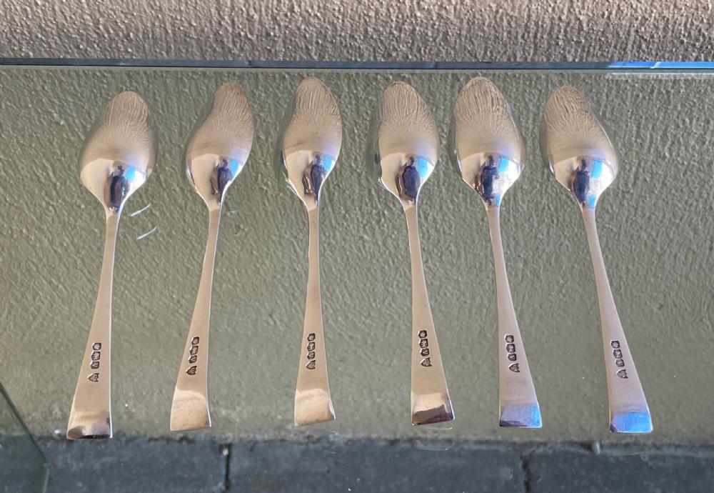 A set of six silver Art Deco grapefruit spoons with geometric tapered handles arranged in a row on a reflective surface. View III