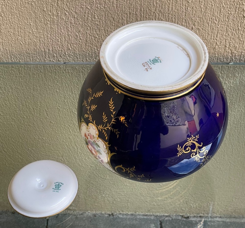 A bulbous cobalt blue porcelain vase with a fitted lid, featuring ornate gilded foliate borders surrounding a central hand-painted landscape cartouche. View V