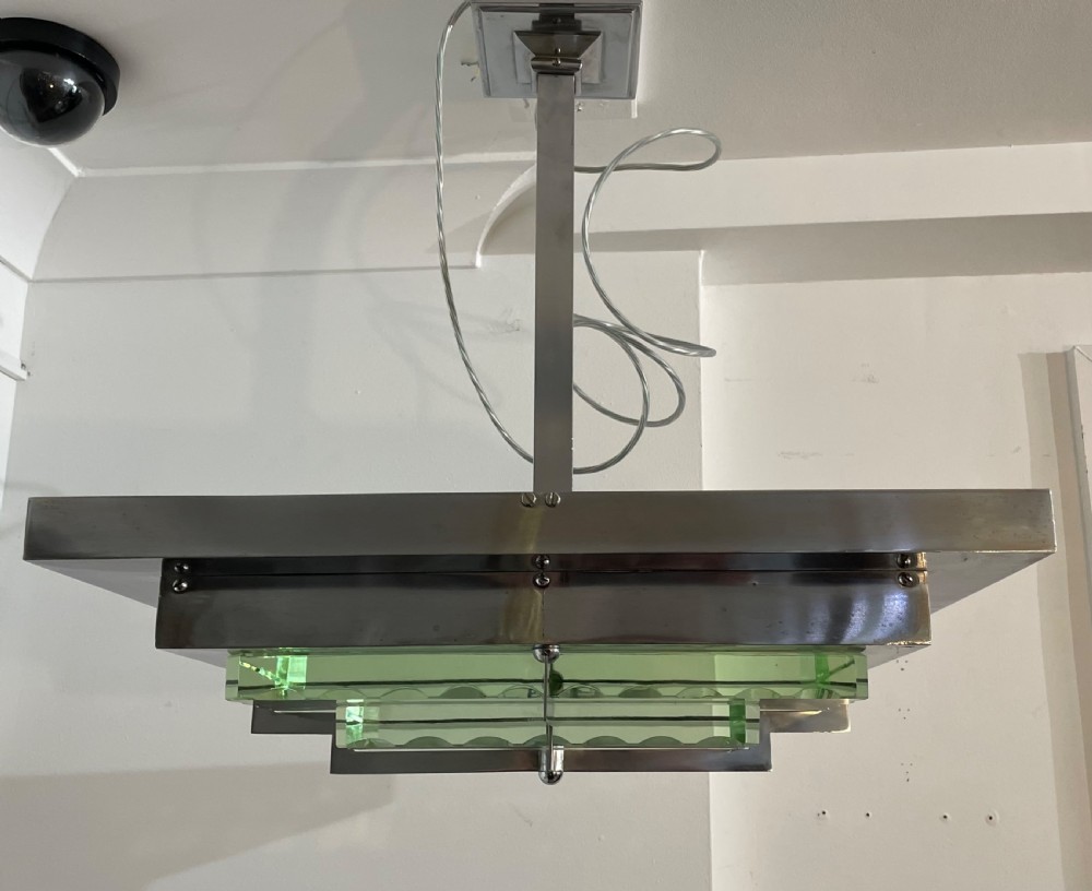 An Art Deco hanging pendant light featuring a tiered chrome-plated metal frame holding layered green glass plates suspended from a central stem.