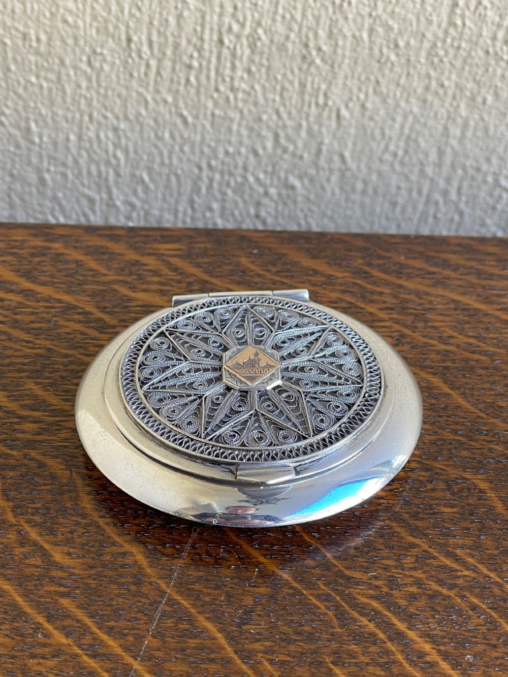 A round silver powder compact displaying intricate filigree wirework across the lid with a central star-shaped pattern.