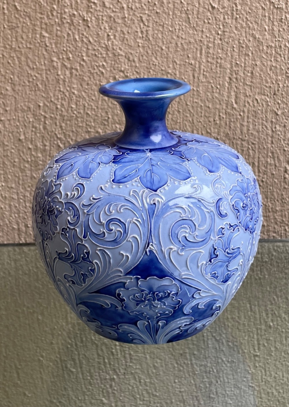 A bulbous blue ceramic vase with raised tubelined floral decoration and a short flared neck.