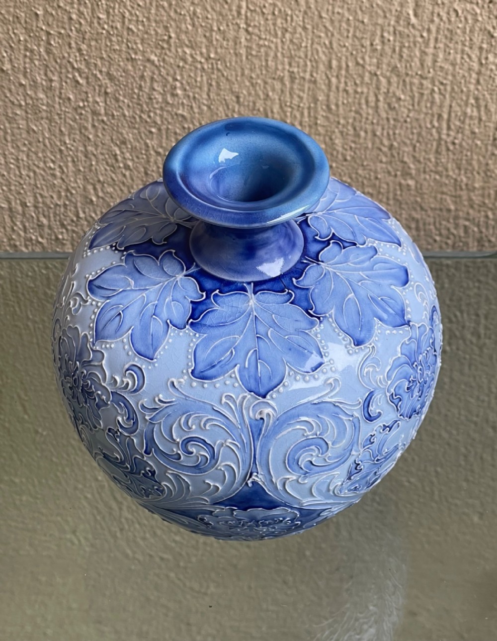 A bulbous blue ceramic vase with raised tubelined floral decoration and a short flared neck. View II