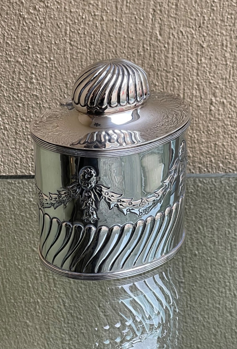 A cylindrical Edwardian sterling silver tea caddy featuring embossed floral garlands and spiral fluting around the lower body. View II