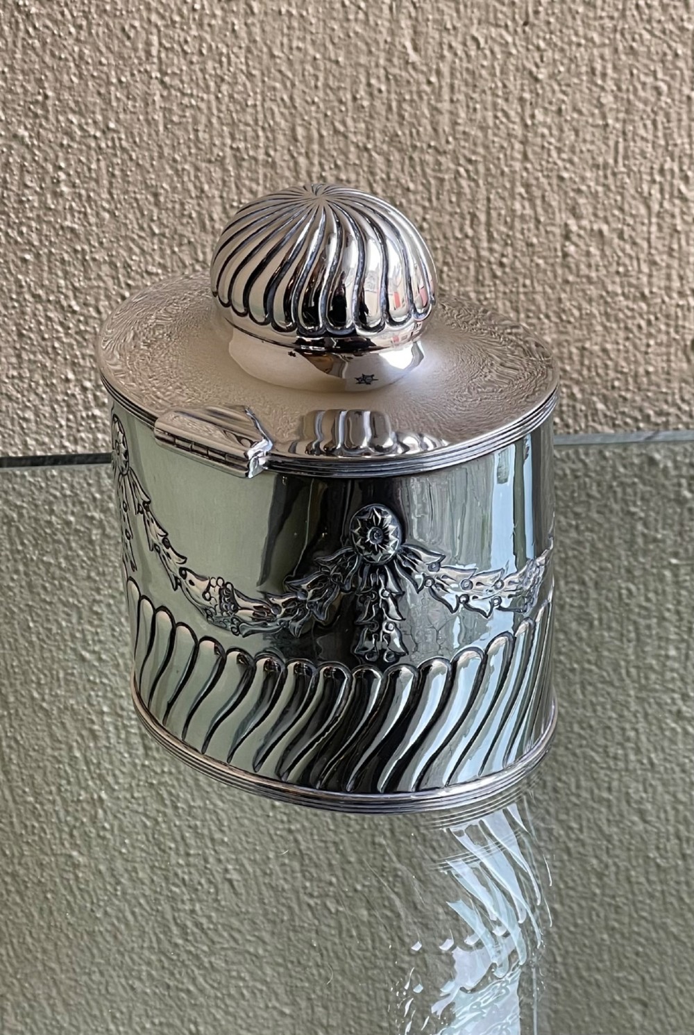 A cylindrical Edwardian sterling silver tea caddy featuring embossed floral garlands and spiral fluting around the lower body. View III
