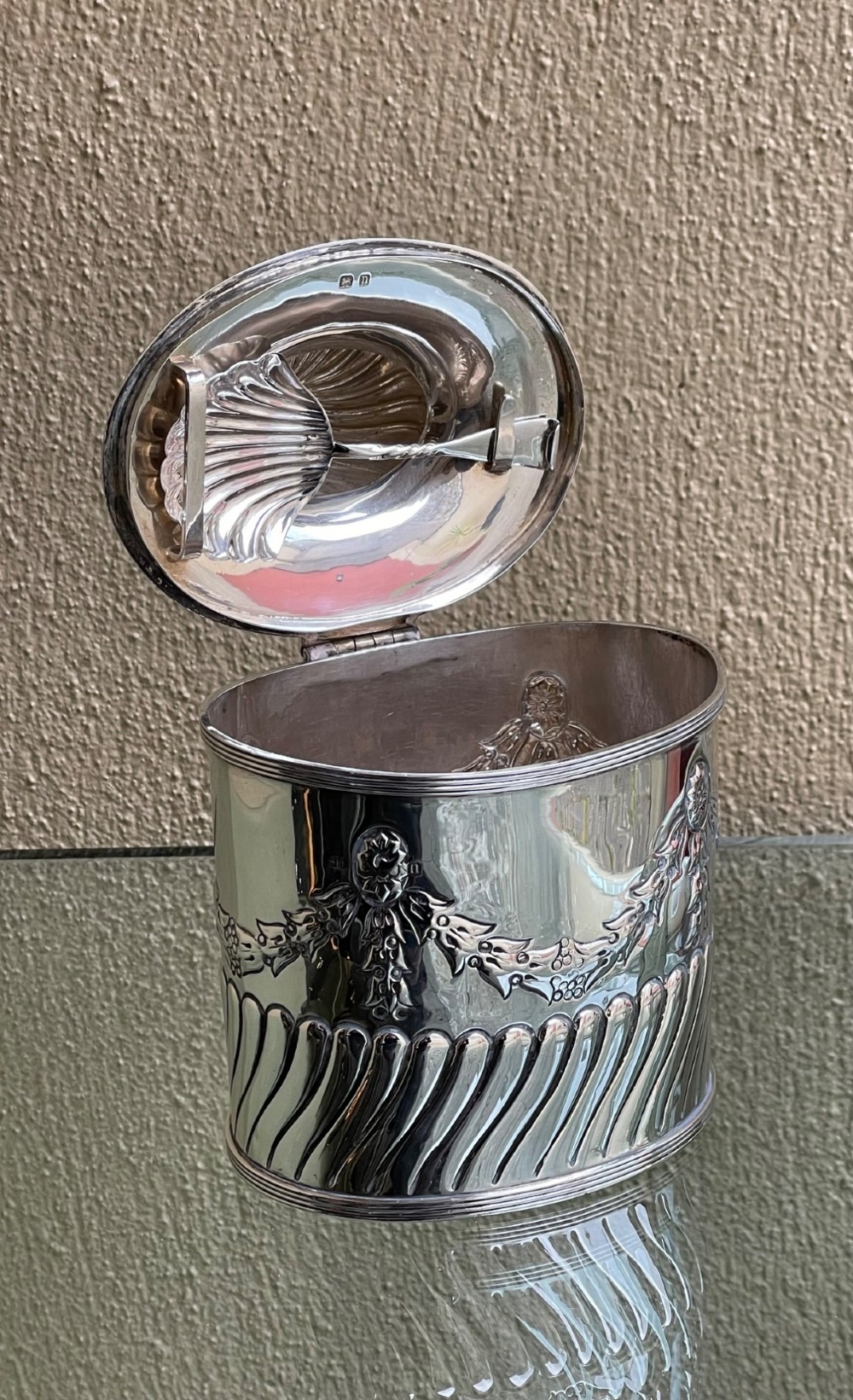 A cylindrical Edwardian sterling silver tea caddy featuring embossed floral garlands and spiral fluting around the lower body. View V
