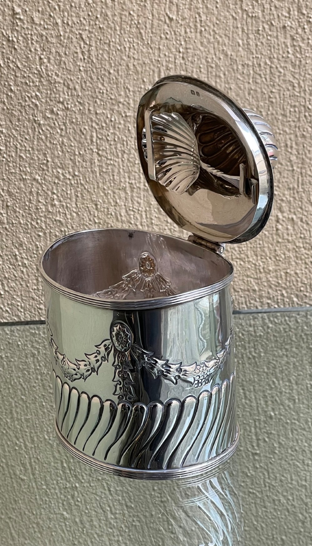 A cylindrical Edwardian sterling silver tea caddy featuring embossed floral garlands and spiral fluting around the lower body. View VI