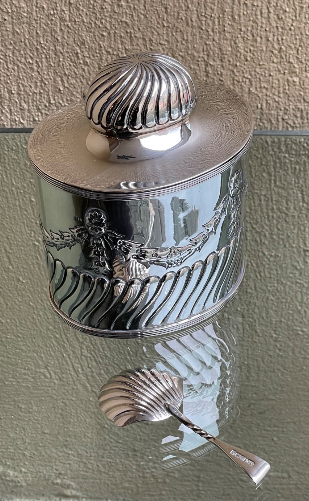 A cylindrical Edwardian sterling silver tea caddy featuring embossed floral garlands and spiral fluting around the lower body. View X