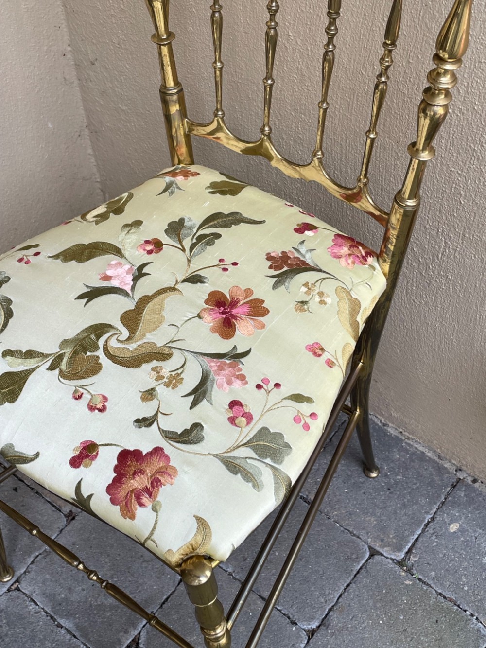 A polished brass Chiavari style salon chair featuring a spindle backrest, ornate cresting rail, turned legs, and a floral upholstered seat. View II