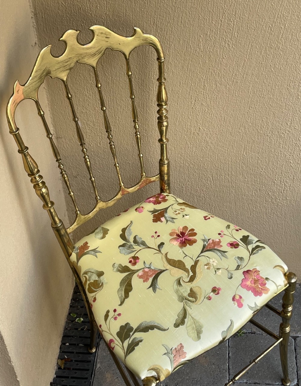 A polished brass Chiavari style salon chair featuring a spindle backrest, ornate cresting rail, turned legs, and a floral upholstered seat. View III